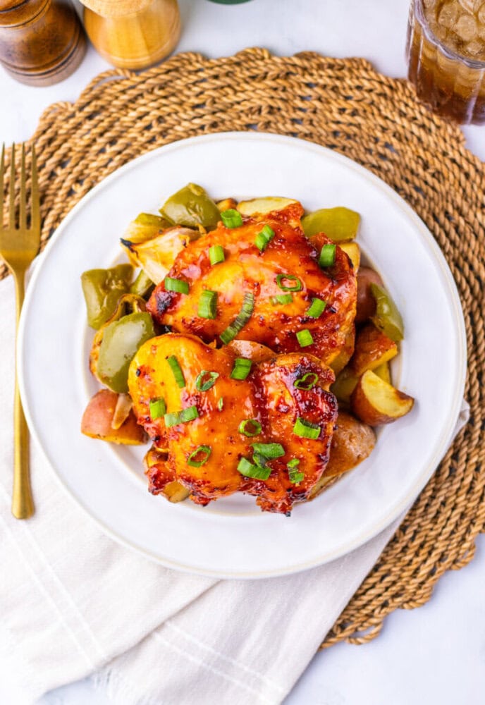 A plate of glazed chicken thighs served with roasted potatoes and green bell peppers, garnished with chopped chives.