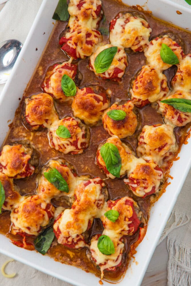 Bell peppers stuffed with meat, topped with melted cheese and basil, baked in a white rectangular dish.