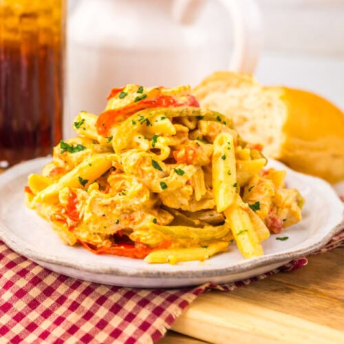 Plate of creamy pasta with peppers and herbs on a checkered cloth, bread and iced drink in the background.