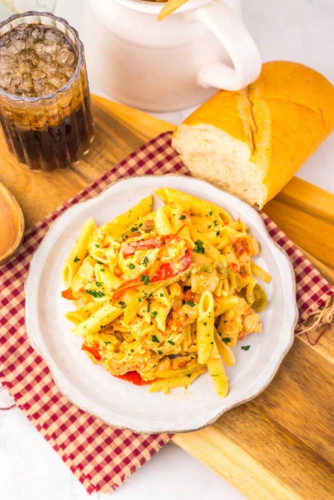 A plate of creamy pasta with vegetables, a slice of bread, and a glass of soda on a checkered napkin.