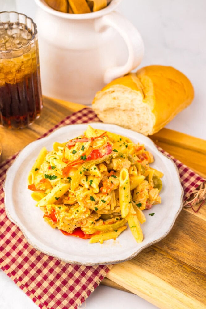 Plate of creamy pasta with chicken and peppers, served with bread and a glass of soda on a checkered napkin.