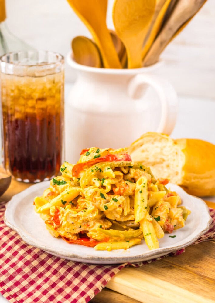 Plate of creamy pasta with tomatoes and herbs, served with bread and a glass of soda on a red checkered napkin.