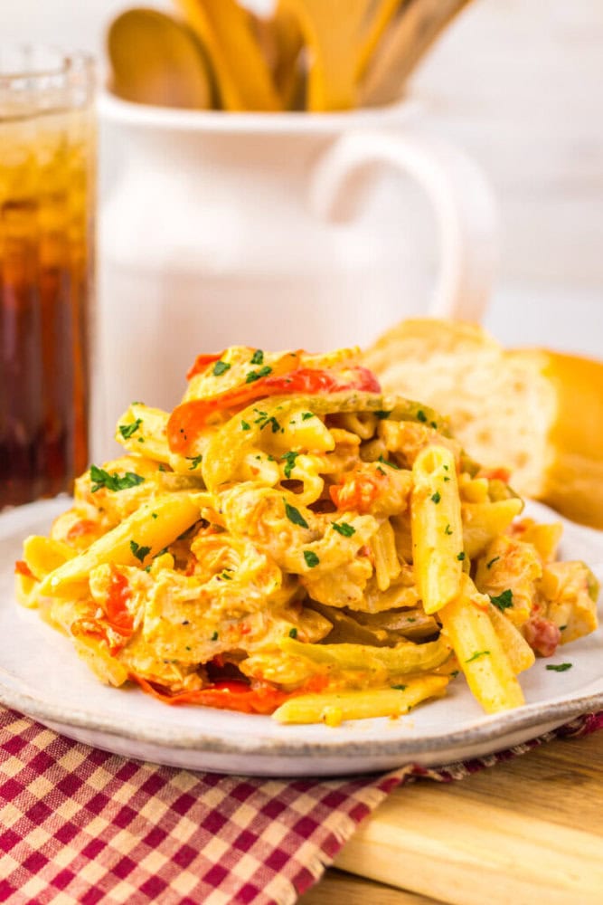 A plate of creamy penne pasta with tomatoes and herbs, served with bread and a drink in the background.