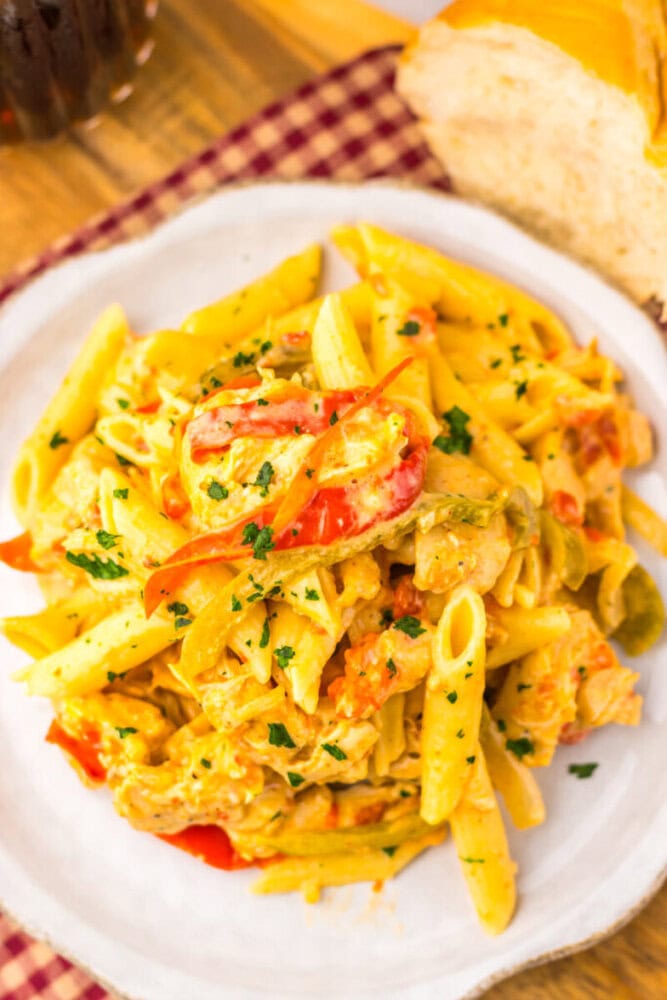 A plate of creamy penne pasta with sliced red peppers and herbs, served next to a piece of bread.