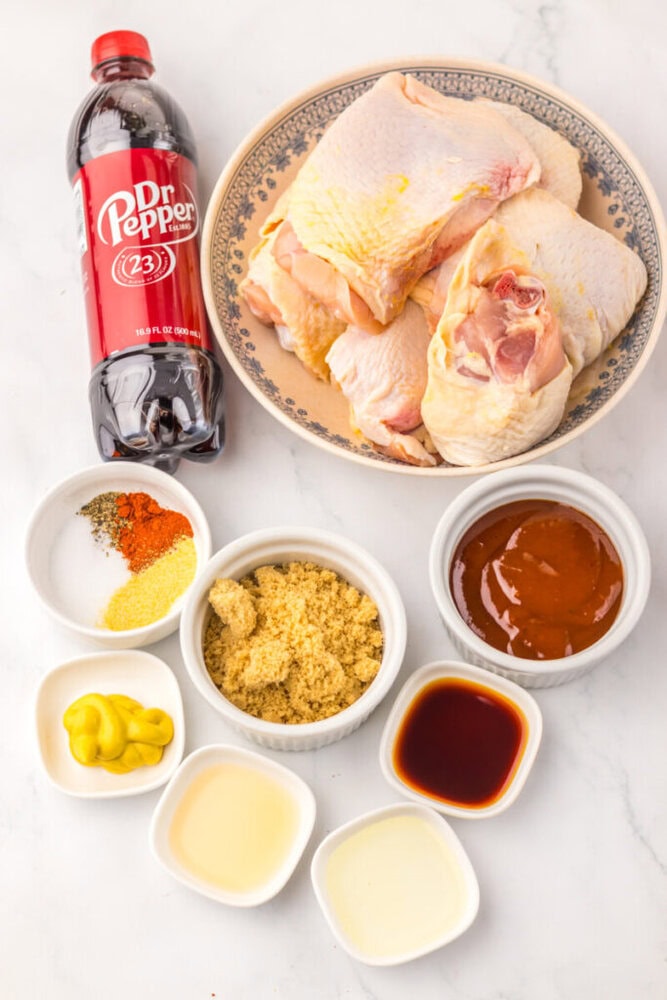 Raw chicken, Dr Pepper, brown sugar, barbecue sauce, mustard, spices, vinegar, and soy sauce on a countertop.