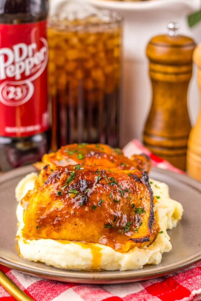 Glazed chicken thighs on mashed potatoes, served with soda and pepper mills in the background.