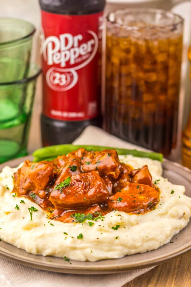 Plate of mashed potatoes topped with saucy meat, with a Dr Pepper bottle and glass in the background.
