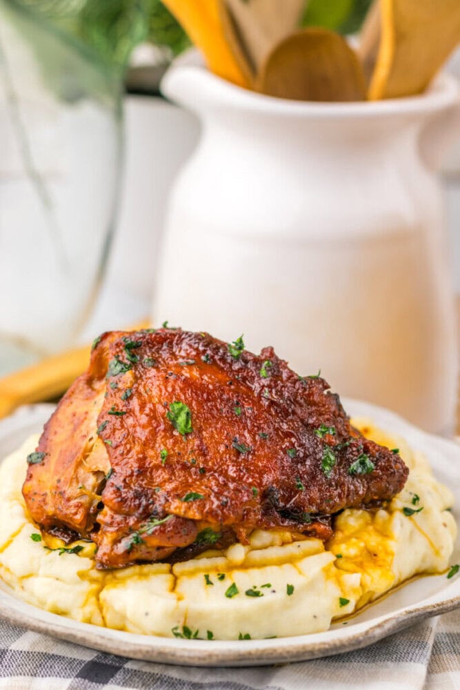 Barbecue chicken thigh garnished with herbs, served on creamy mashed potatoes on a plate.