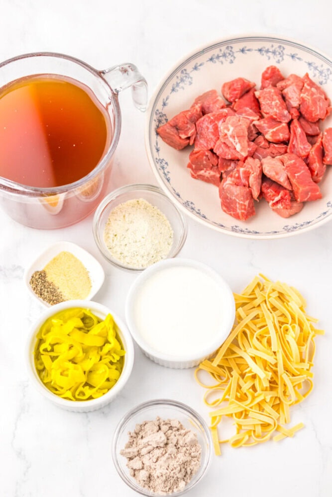 Ingredients for a beef noodle dish: raw beef, broth, egg noodles, pepperoncini, seasonings, milk, and powder mix.