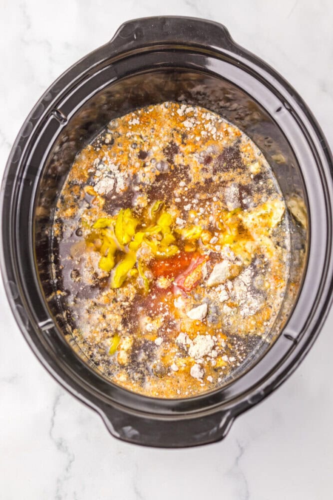 Ingredients, including seasonings and peppers, in a slow cooker ready to be mixed and cooked.