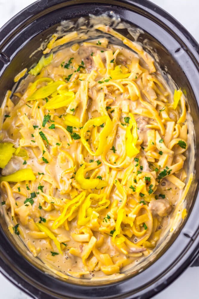 Creamy pasta with yellow pepper slices and herbs in a black slow cooker.