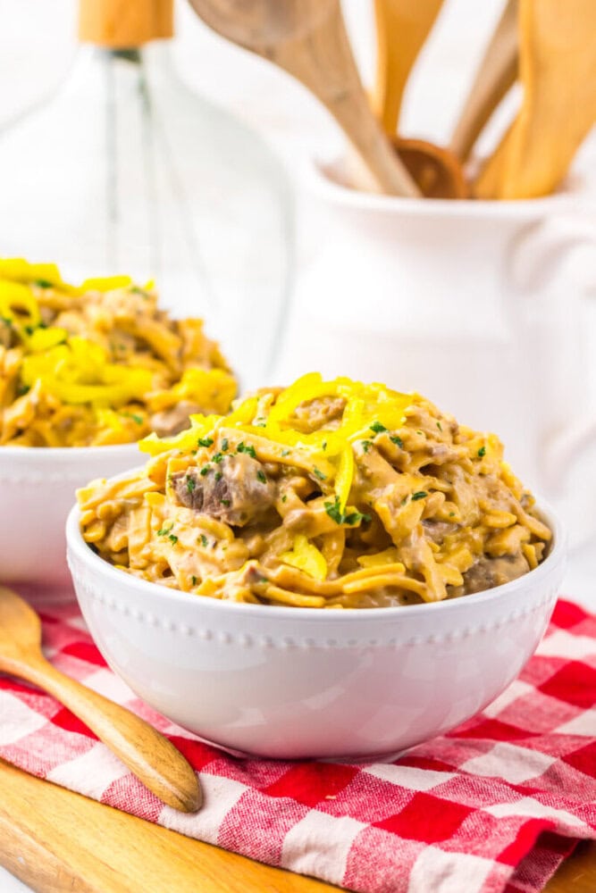 Creamy pasta with ground beef and sliced yellow peppers served in a white bowl on a red checkered cloth.