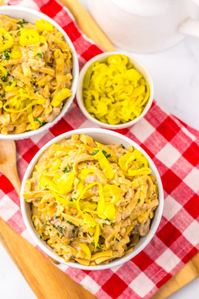Bowls of creamy pasta topped with sliced yellow peppers on a red and white checkered cloth.