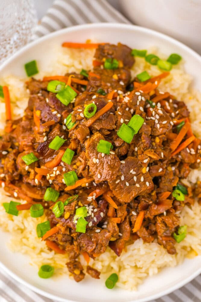 A plate of beef stir-fry with carrots, rice, sesame seeds, and chopped green onions.