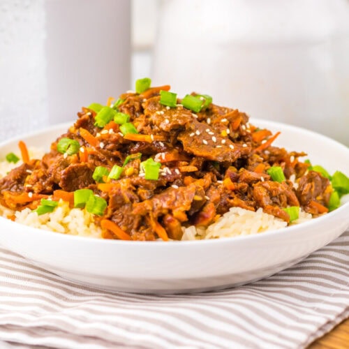 A bowl of beef stir-fry with rice, topped with green onions and sesame seeds, on a striped napkin.