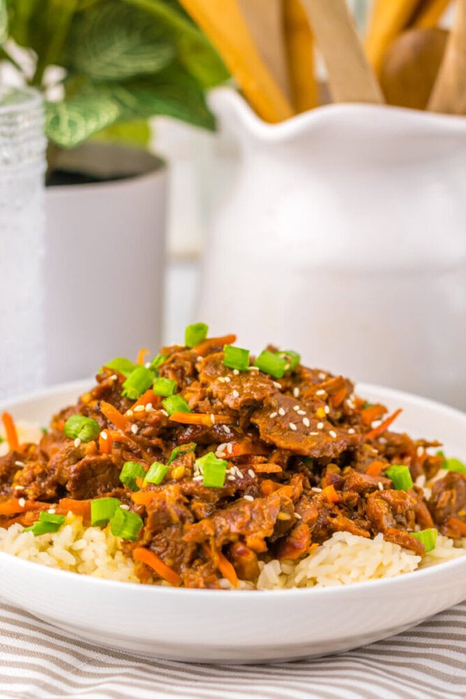 Shredded beef with chopped green onions and sesame seeds served over rice in a white bowl.