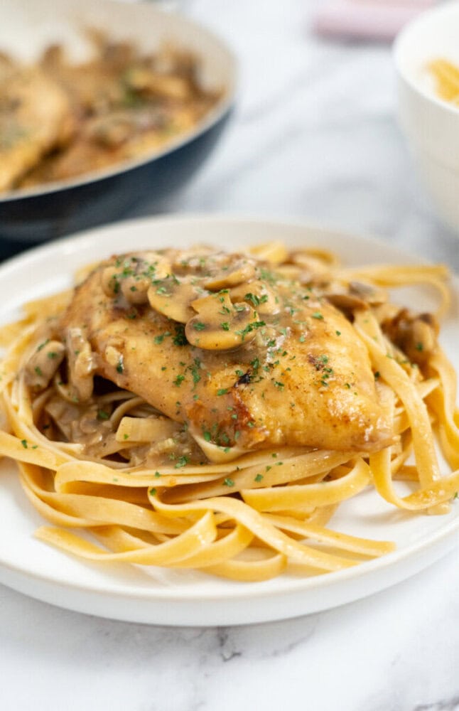 Chicken breast with mushroom sauce served over fettuccine pasta on a white plate.