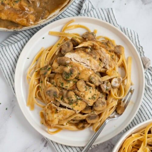 Plate of pasta topped with sliced chicken breast and creamy mushroom sauce, served with a fork on the side.