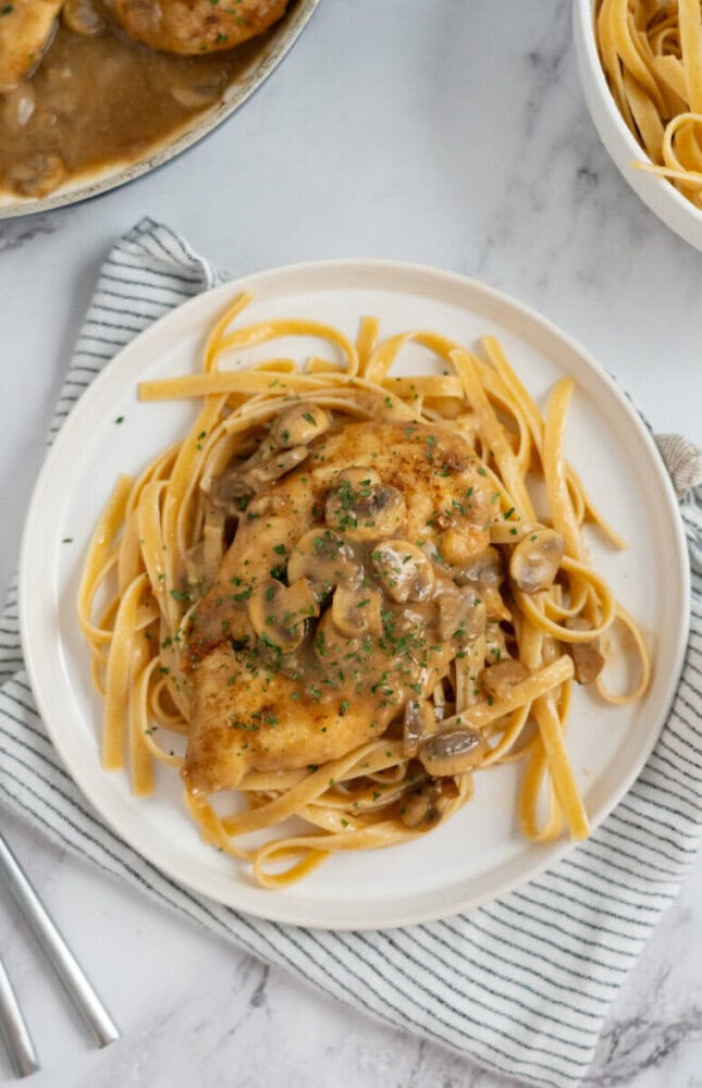 A plate of pasta topped with chicken breast and creamy mushroom sauce, garnished with chopped herbs.