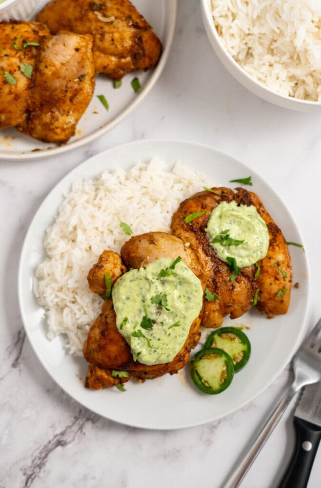 A plate of rice and seasoned chicken topped with green sauce, garnished with herbs and sliced jalapeños.