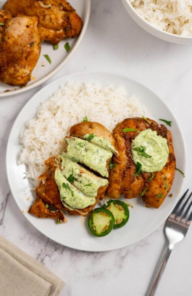 A plate of white rice and grilled chicken topped with green sauce, garnished with sliced jalapeños.