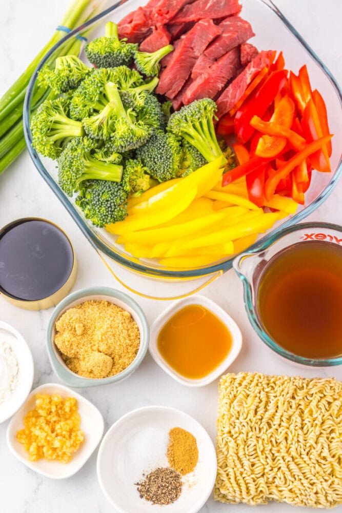 Glass dish with sliced beef, broccoli, red and yellow peppers. Surrounding bowls hold broth, sauces, ramen, and seasonings.
