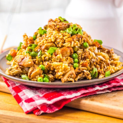 Plate of fried rice with vegetables and chicken, garnished with green onions, on a red checkered napkin.