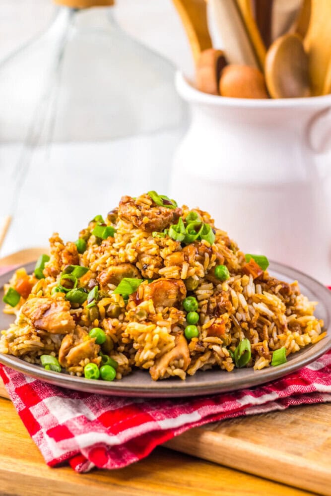 A plate of fried rice with chicken, peas, carrots, and green onions, on a red checkered napkin.
