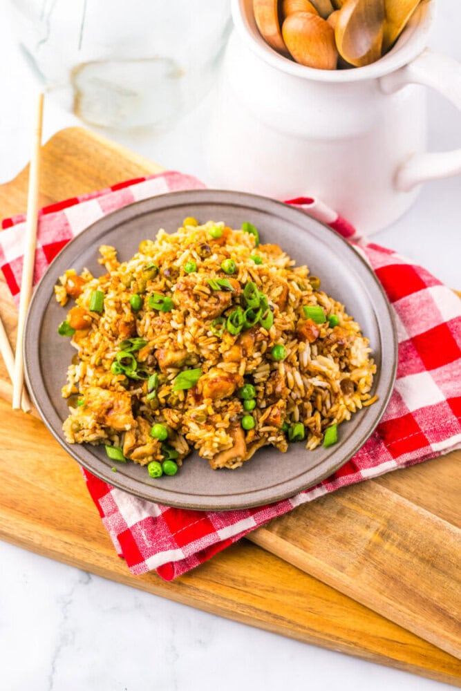 A plate of fried rice with vegetables and chicken, garnished with green onions, on a red checkered napkin.