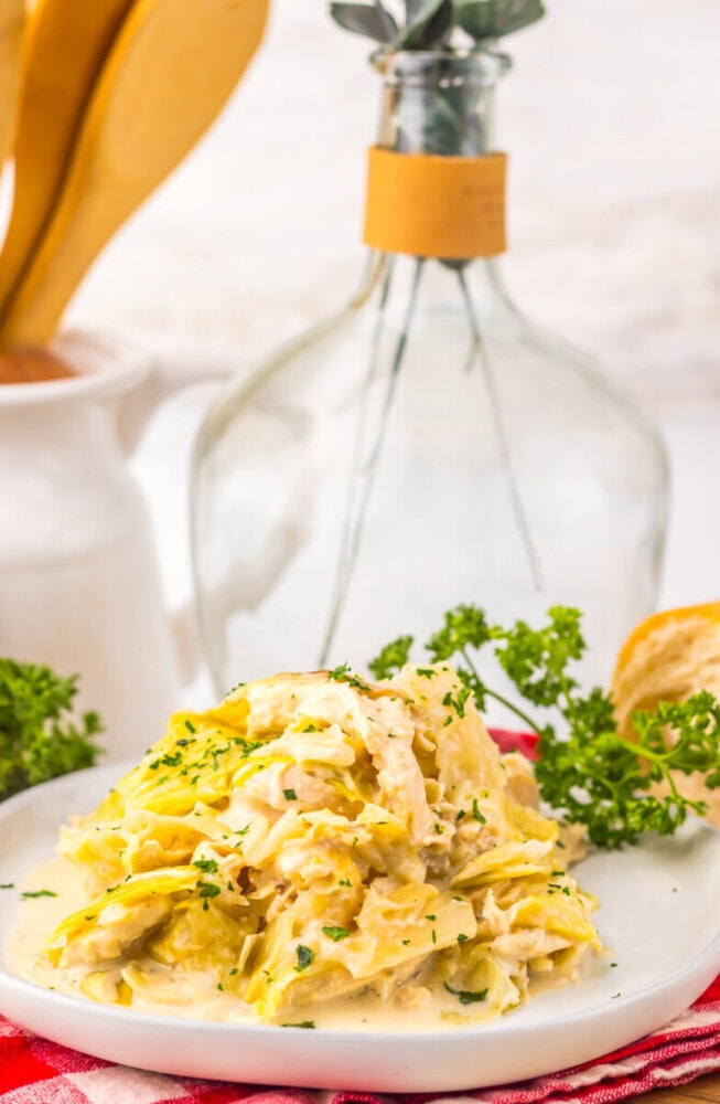 Creamy pasta salad garnished with parsley on a white plate, with bread and a glass bottle in the background.