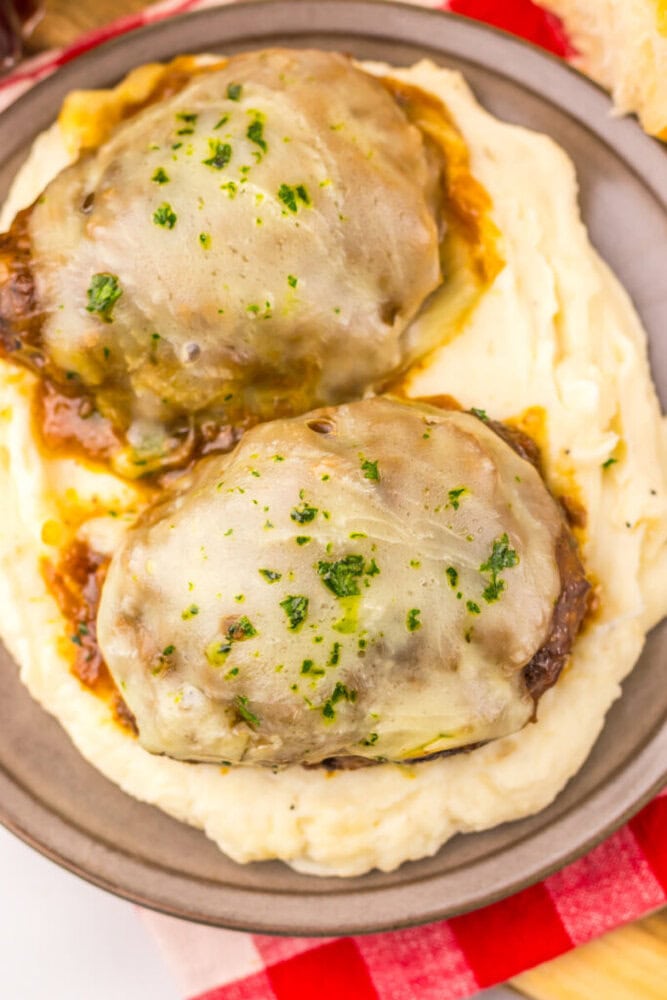 Two cheesy meatloaf patties topped with herbs served on a bed of creamy mashed potatoes on a plate.