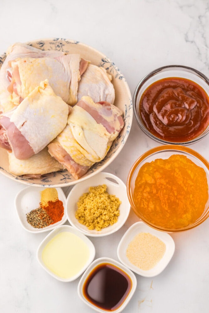 Raw chicken pieces, barbecue sauce, apricot preserves, spices, oil, brown sugar, and soy sauce on a white surface.