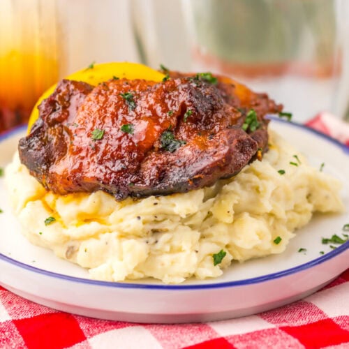 BBQ glazed pork chop with peach slice atop creamy mashed potatoes on a white plate with blue rim.