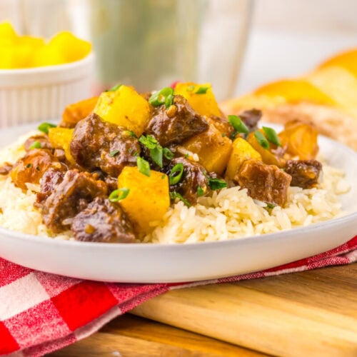 A plate of beef stew with potatoes and rice, garnished with green onions, on a red checkered napkin.