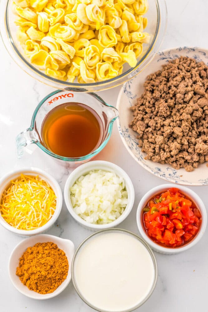 Bowls of tortellini, ground meat, shredded cheese, chopped onions, diced tomatoes, cream, broth, and seasoning.