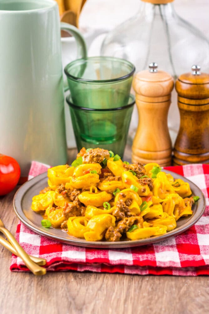 A plate of cheesy macaroni with ground beef and green onions, on a red checkered napkin.