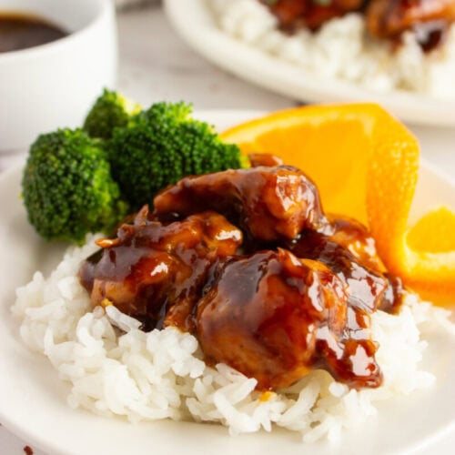 A plate of white rice topped with glazed chicken, broccoli, and orange slices.