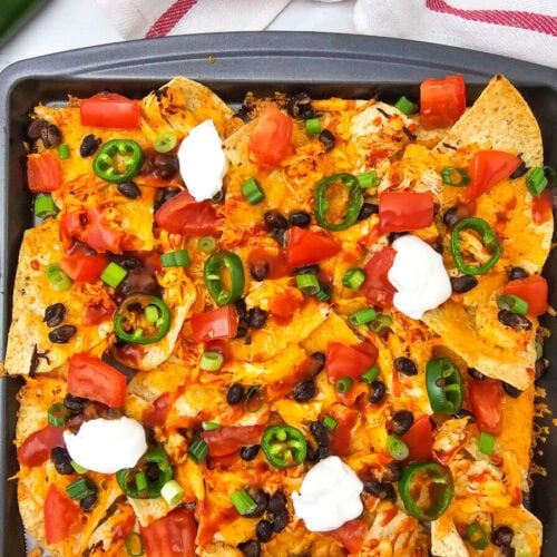 Sheet pan chicken nachos with cheese, jalape&ntilde;os, black beans, and sour cream toppings