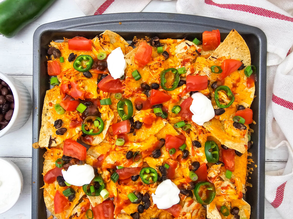 Sheet pan chicken nachos with cheese, jalape&ntilde;os, black beans, and sour cream toppings