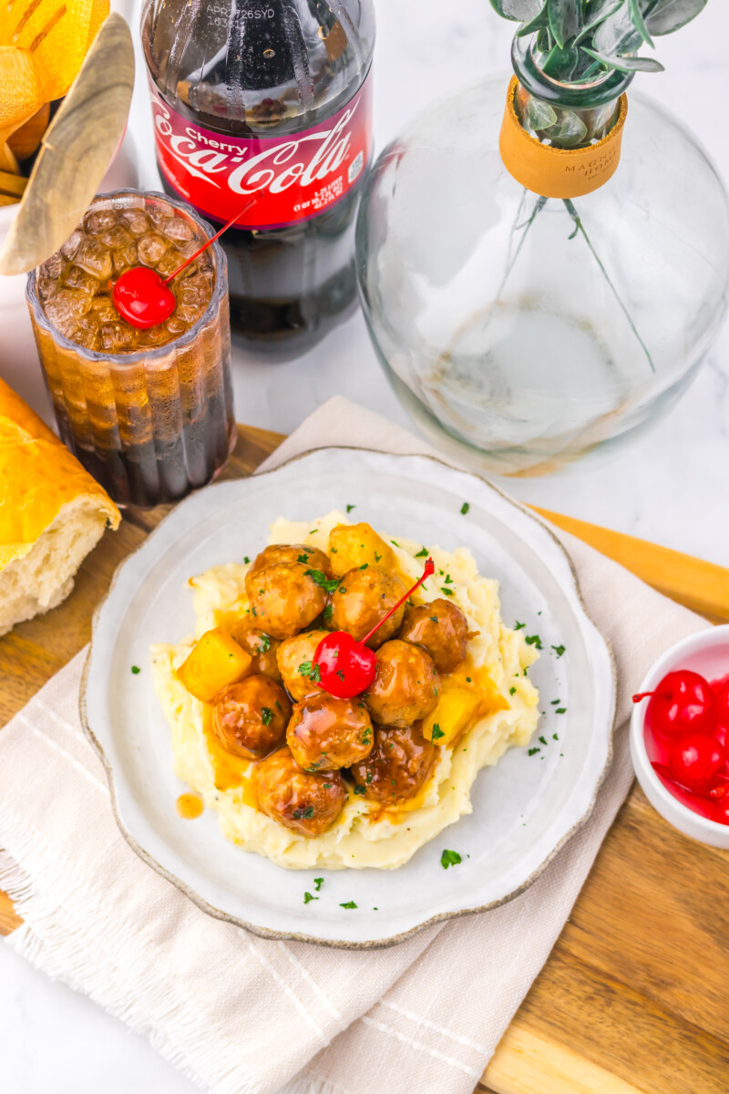Slow cooker cherry cola pineapple BBQ meatballs plated over mashed potatoes with garnish