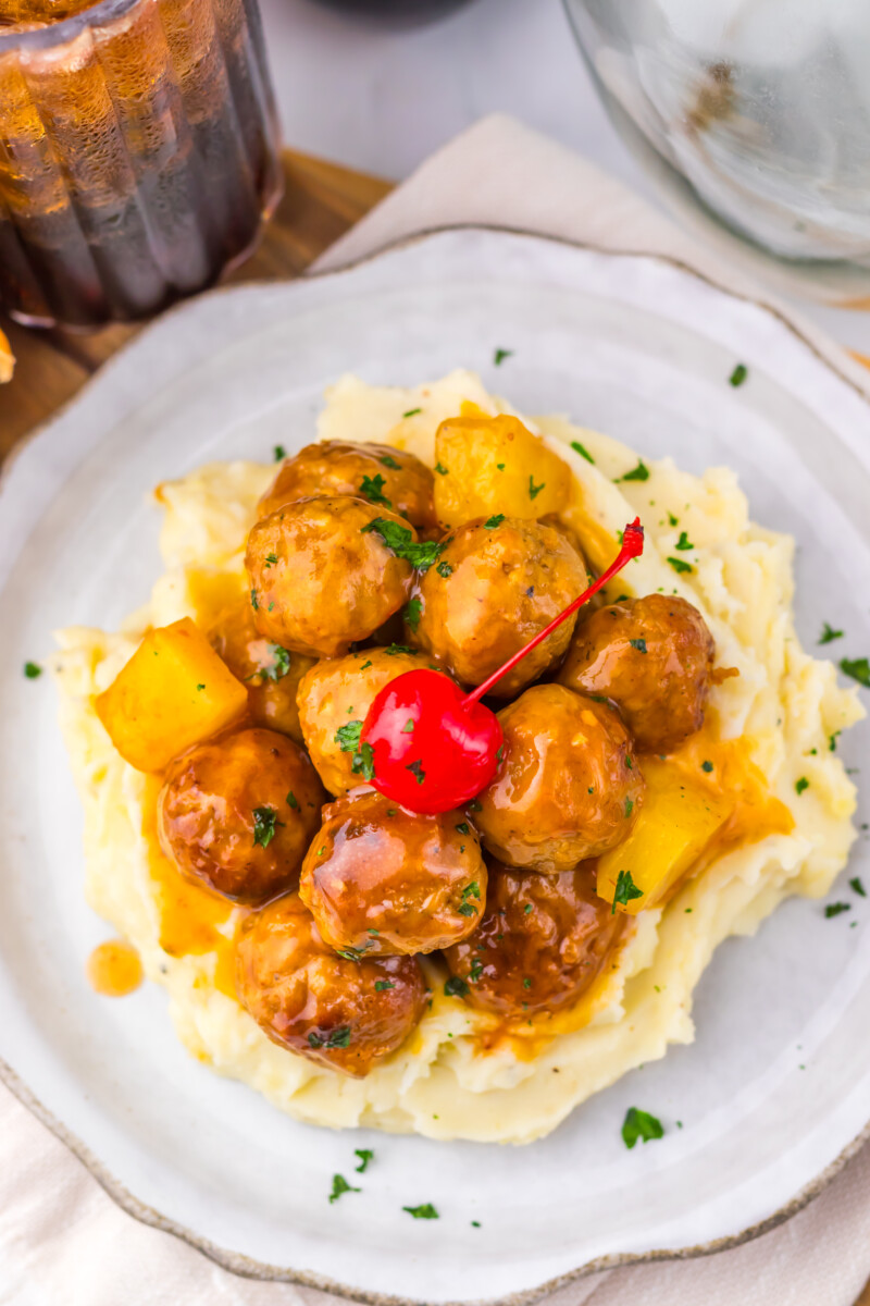 Slow cooker cherry cola pineapple BBQ meatballs served over mashed potatoes with pineapple and cherry garnish