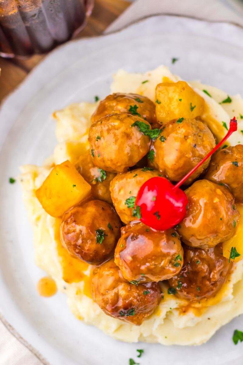 Slow cooker cherry cola pineapple BBQ meatballs served over mashed potatoes with pineapple garnish