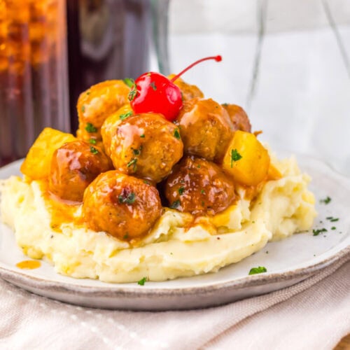 Slow cooker cherry cola pineapple BBQ meatballs served on mashed potatoes with maraschino cherry garnish