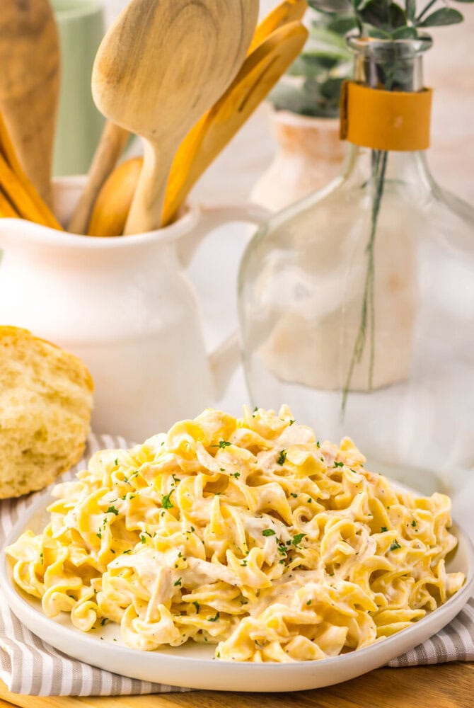 Slow cooker creamy garlic chicken and noodles served on a white plate with chive garnish