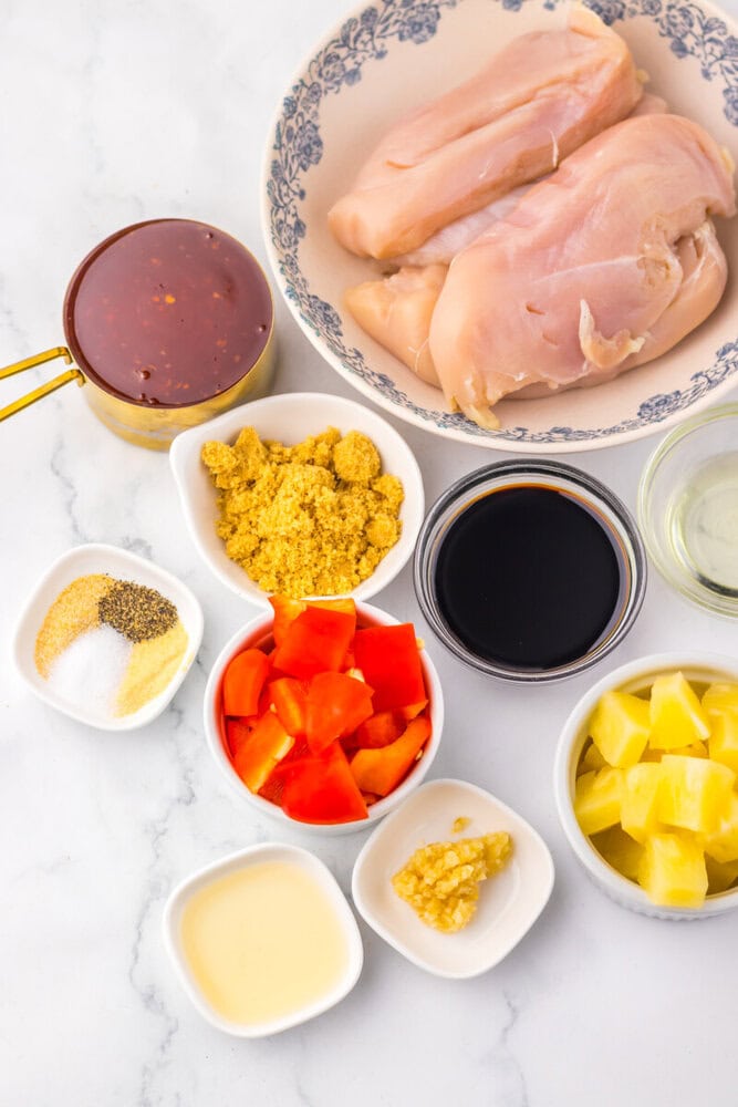 Slow cooker sweet chili pineapple chicken ingredients laid out and ready to cook including raw chicken, pineapple chunks, red peppers, and sauce