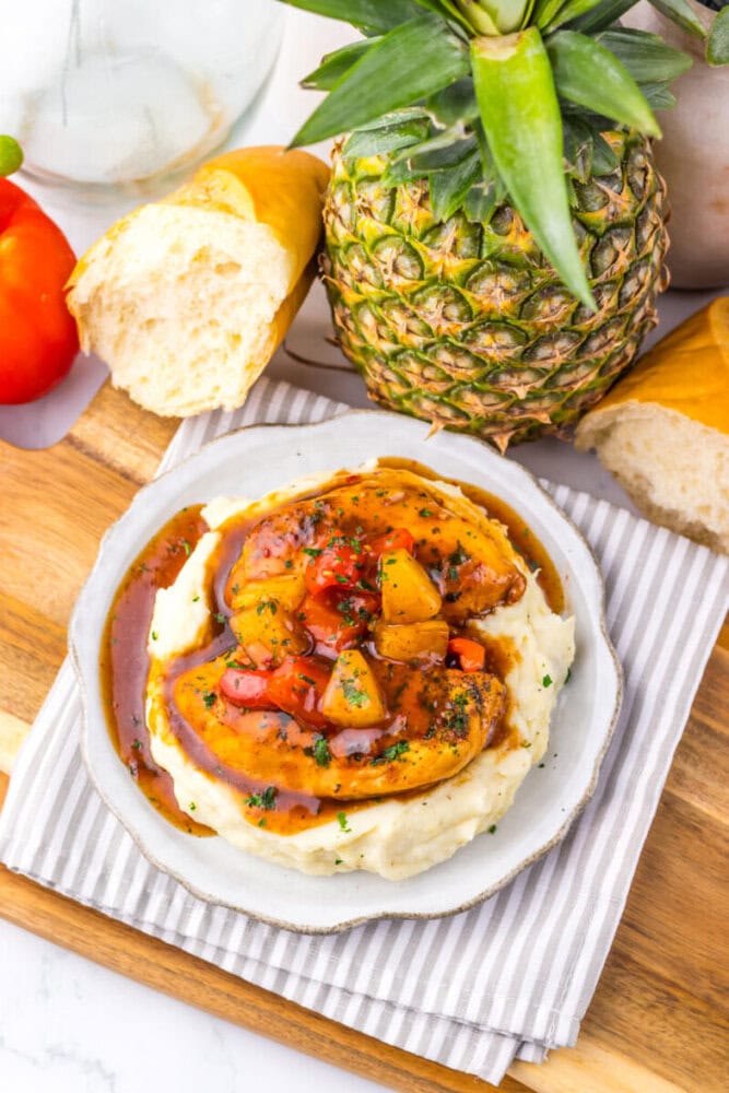 Slow cooker sweet chili pineapple chicken served over creamy mashed potatoes with fresh pineapple and red pepper garnish