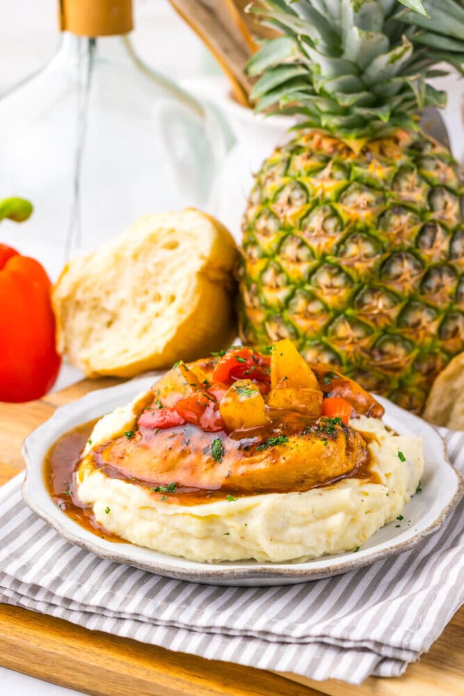 Slow cooker sweet chili pineapple chicken with mashed potatoes and pineapple salsa topping on a white plate