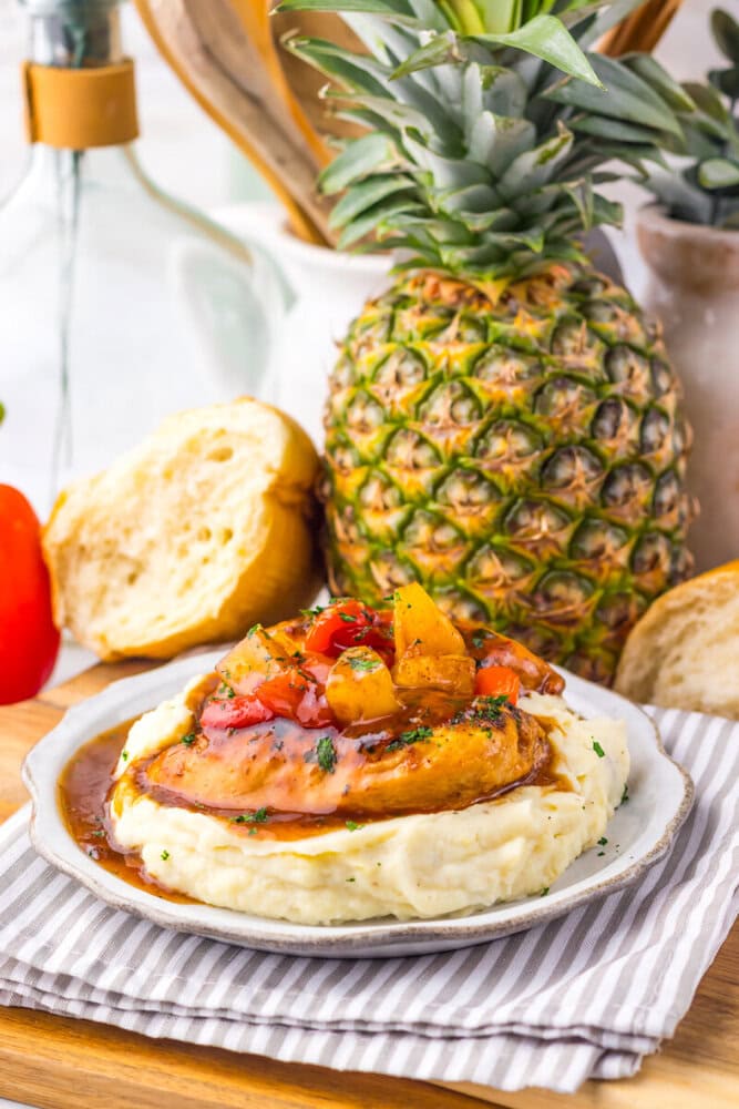 Slow cooker sweet chili pineapple chicken on mashed potatoes with pineapple topping and fresh pineapple in background