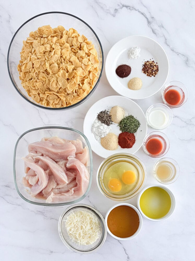 Ingredients for crunchy baked chicken tenders with chili honey arranged in bowls and glasses on marble background