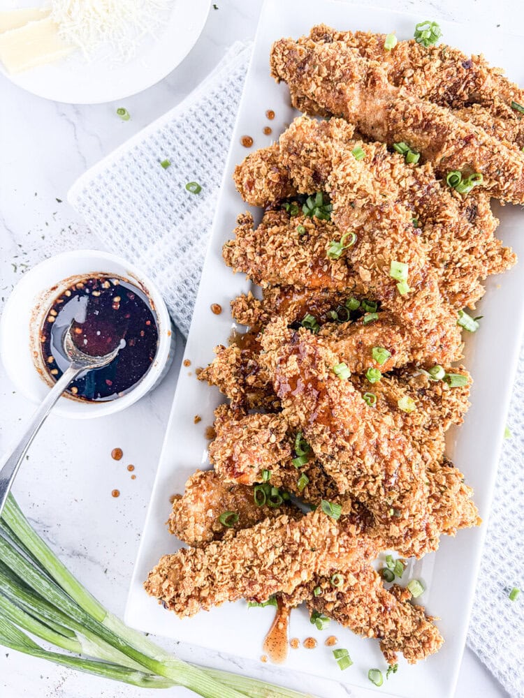 Crunchy baked chicken tenders with chili honey sauce and green onion garnish on white plate